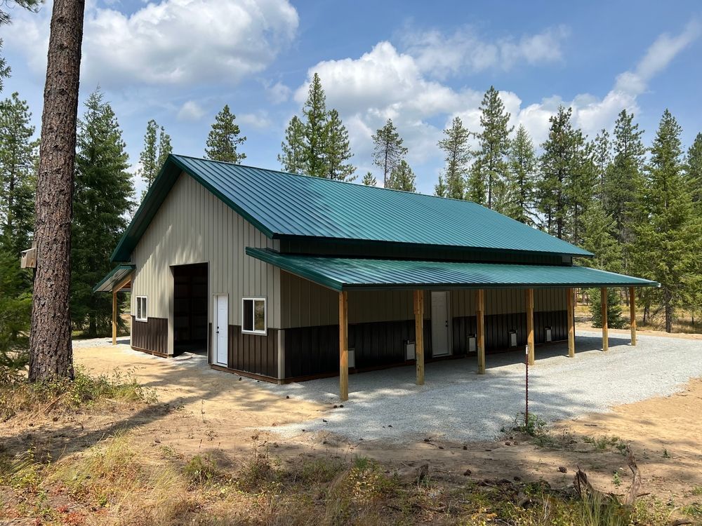 Small beige barn with green metal roof and covered porch in a wooded rural setting