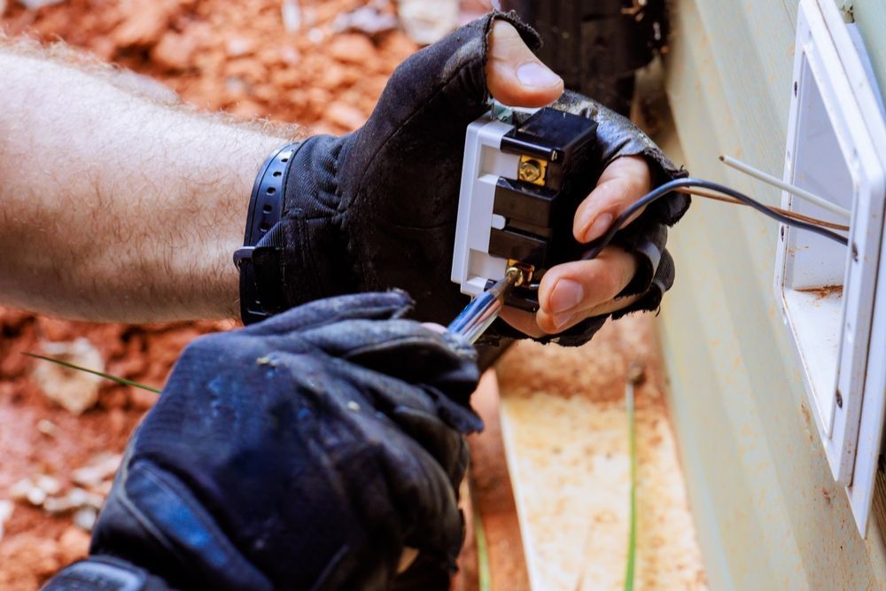 Gloved hands wiring an electrical outlet on an exterior wall