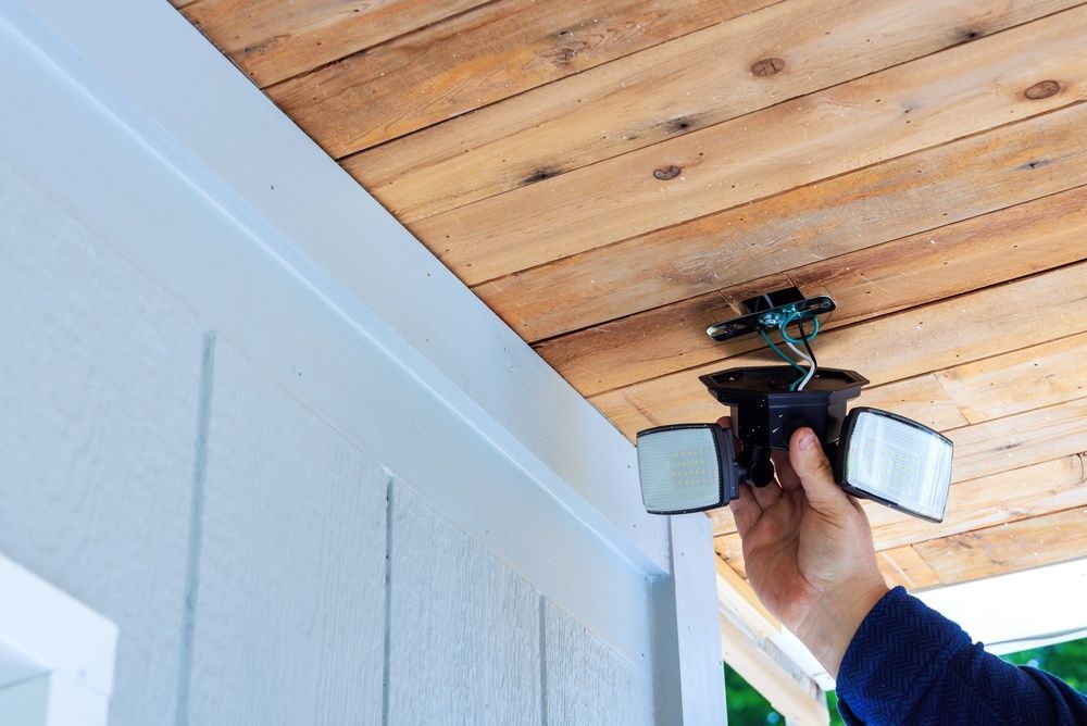 Hand holding a ceiling-mounted light fixture with two side panels in a room with a wooden ceiling