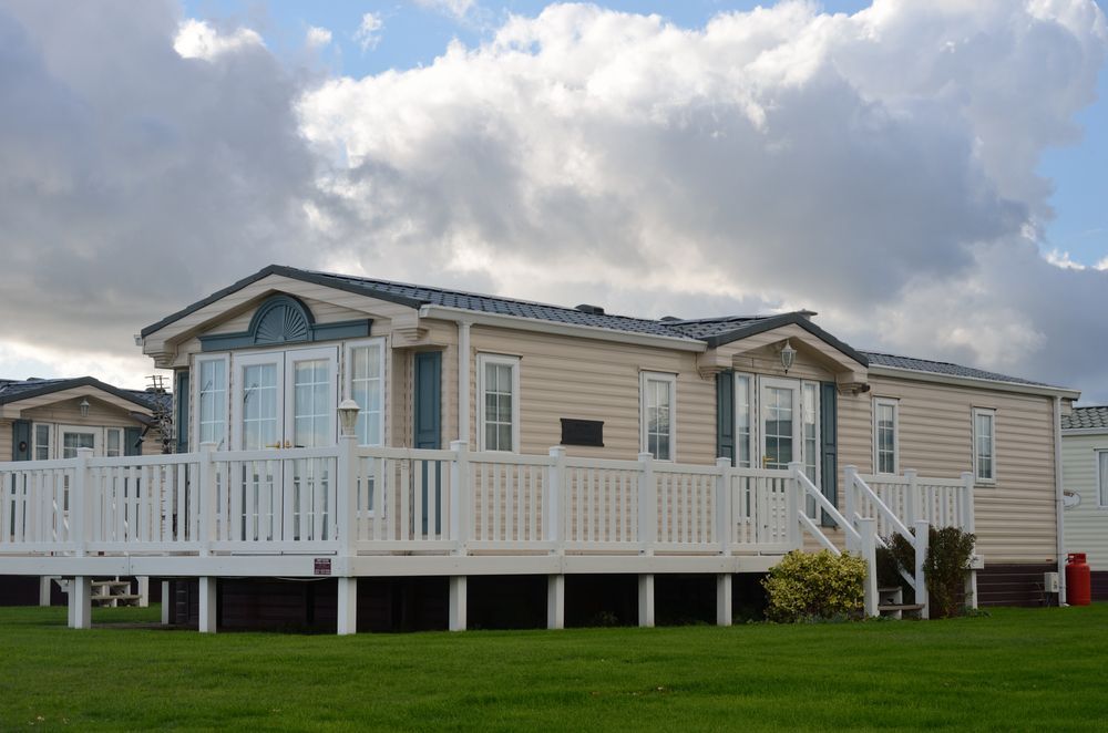 White mobile home with a raised porch and white railing on a grassy lot under cloudy skies