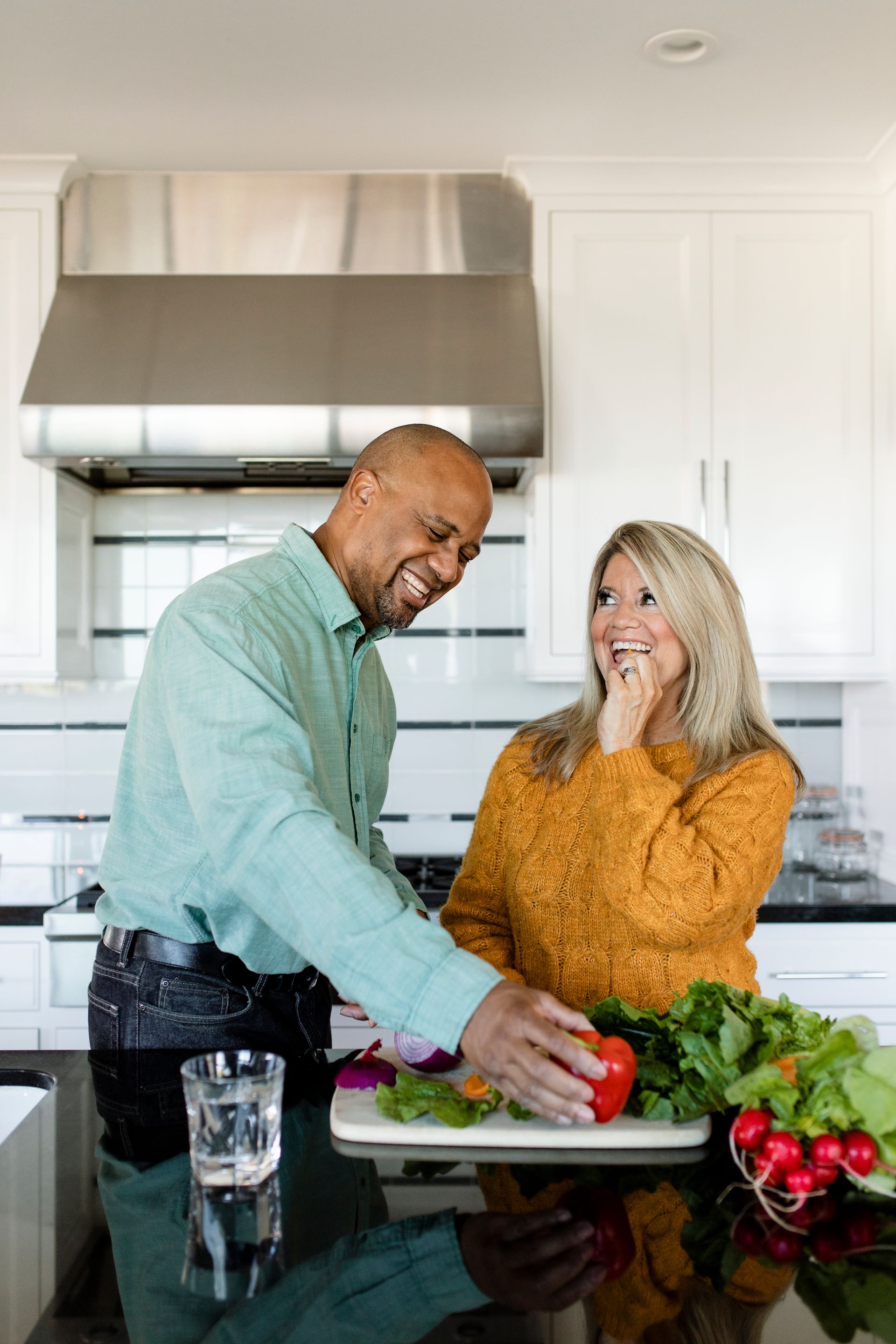 a man is helping a woman cut vegetables in a kitchen .