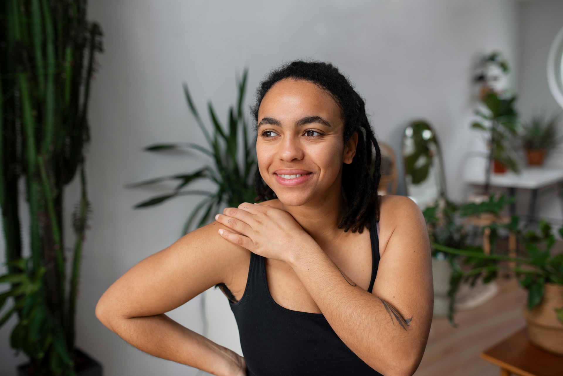 a woman in a black tank top is standing in a room with plants .