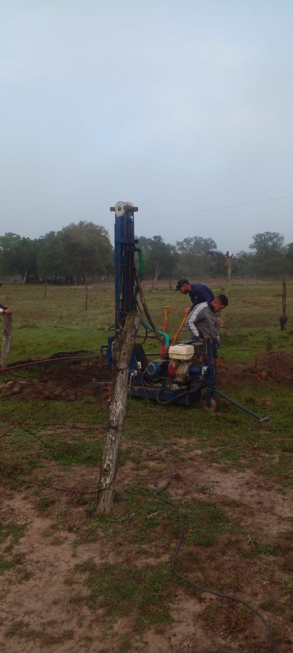 Persona operando una bomba manual en un campo fangoso bajo un cielo nublado.