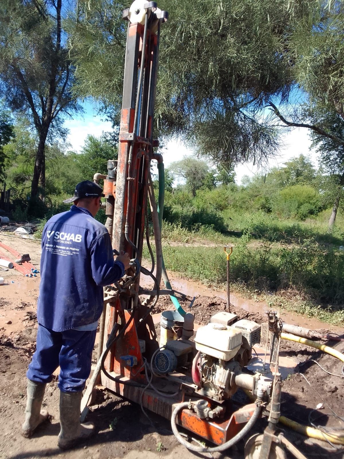 Trabajador operando una plataforma de perforación en una zona boscosa al aire libre.
