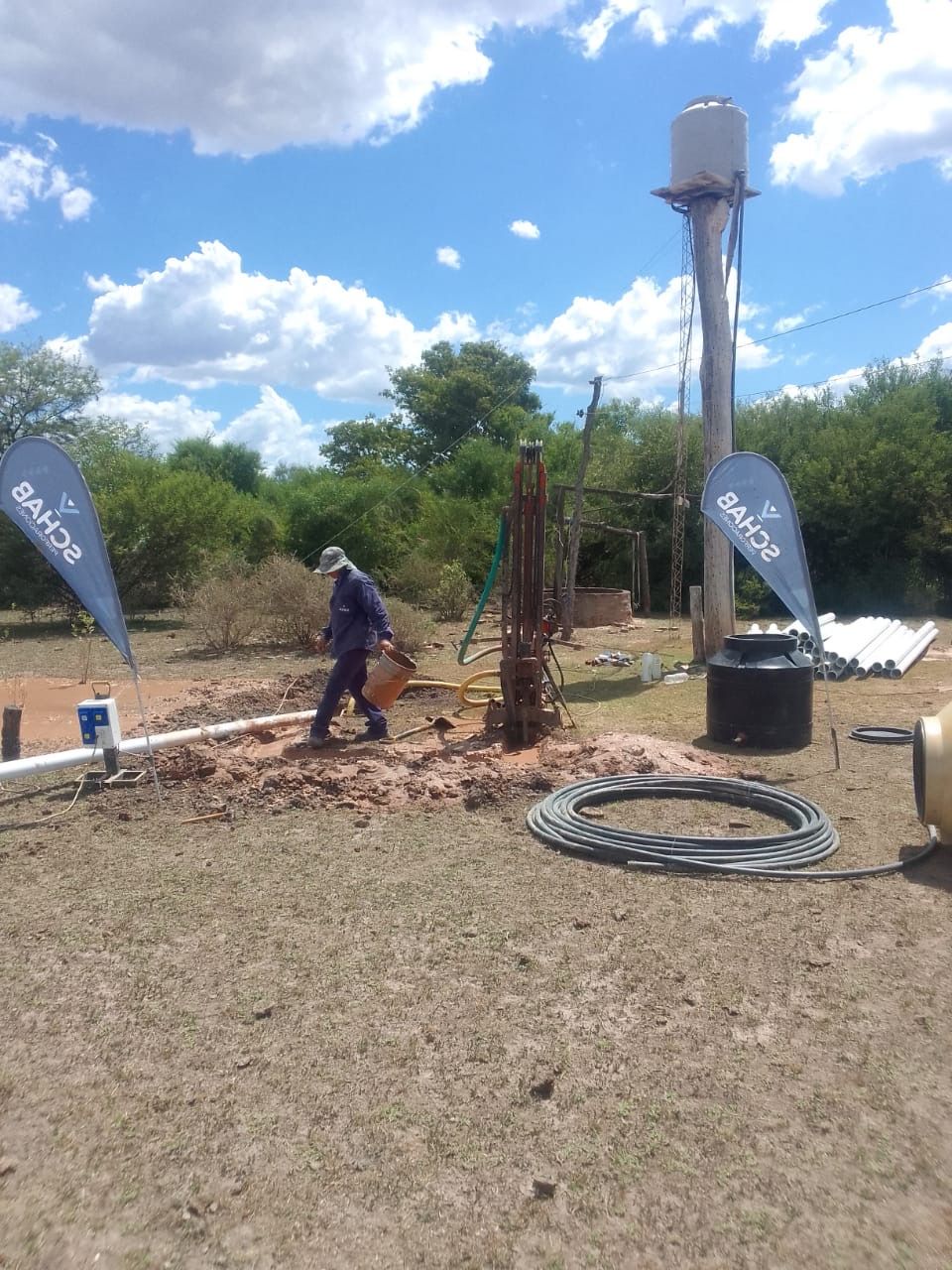Trabajador en un sitio de perforación al aire libre junto a un gran tanque de agua bajo un cielo azul.