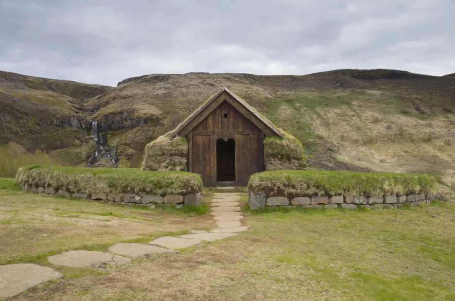 A small wooden house is sitting in the middle of a grassy field.