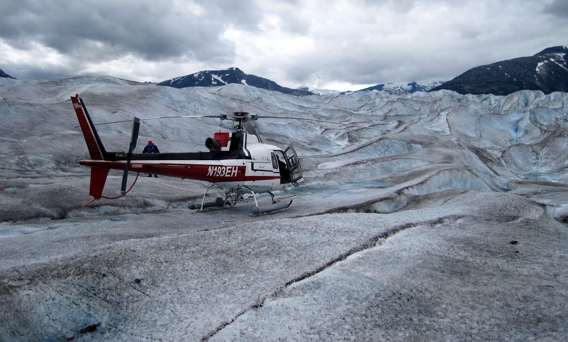 A red and white helicopter is sitting on top of a snow covered field.