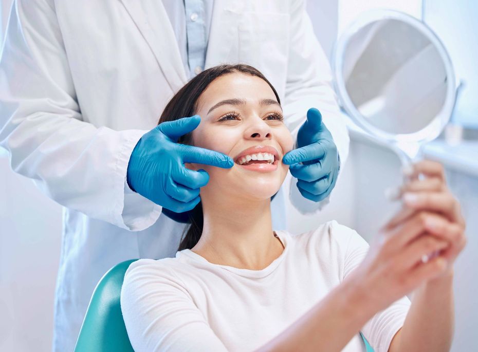 Dentist examining a smiling patient’s teeth with blue gloves in a bright clinic