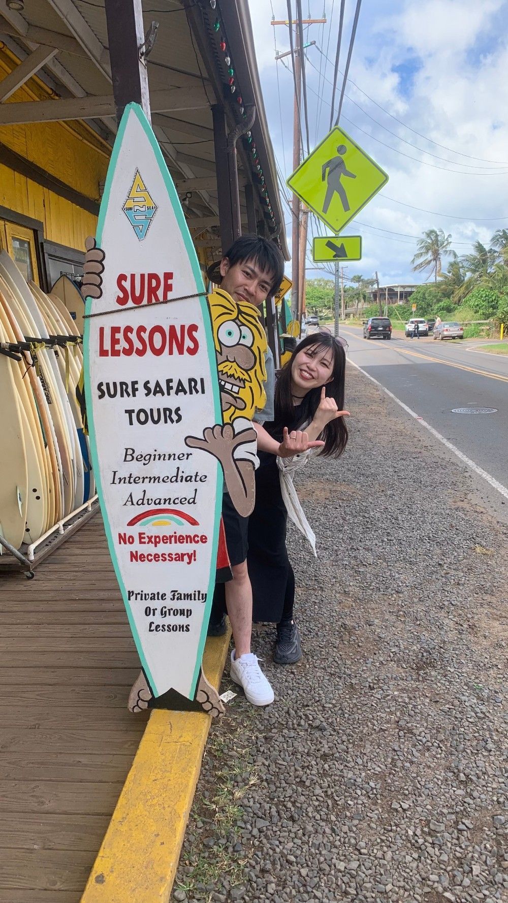 Two people having fun with a surfboard sign that highlights the offerings of a surf shop.