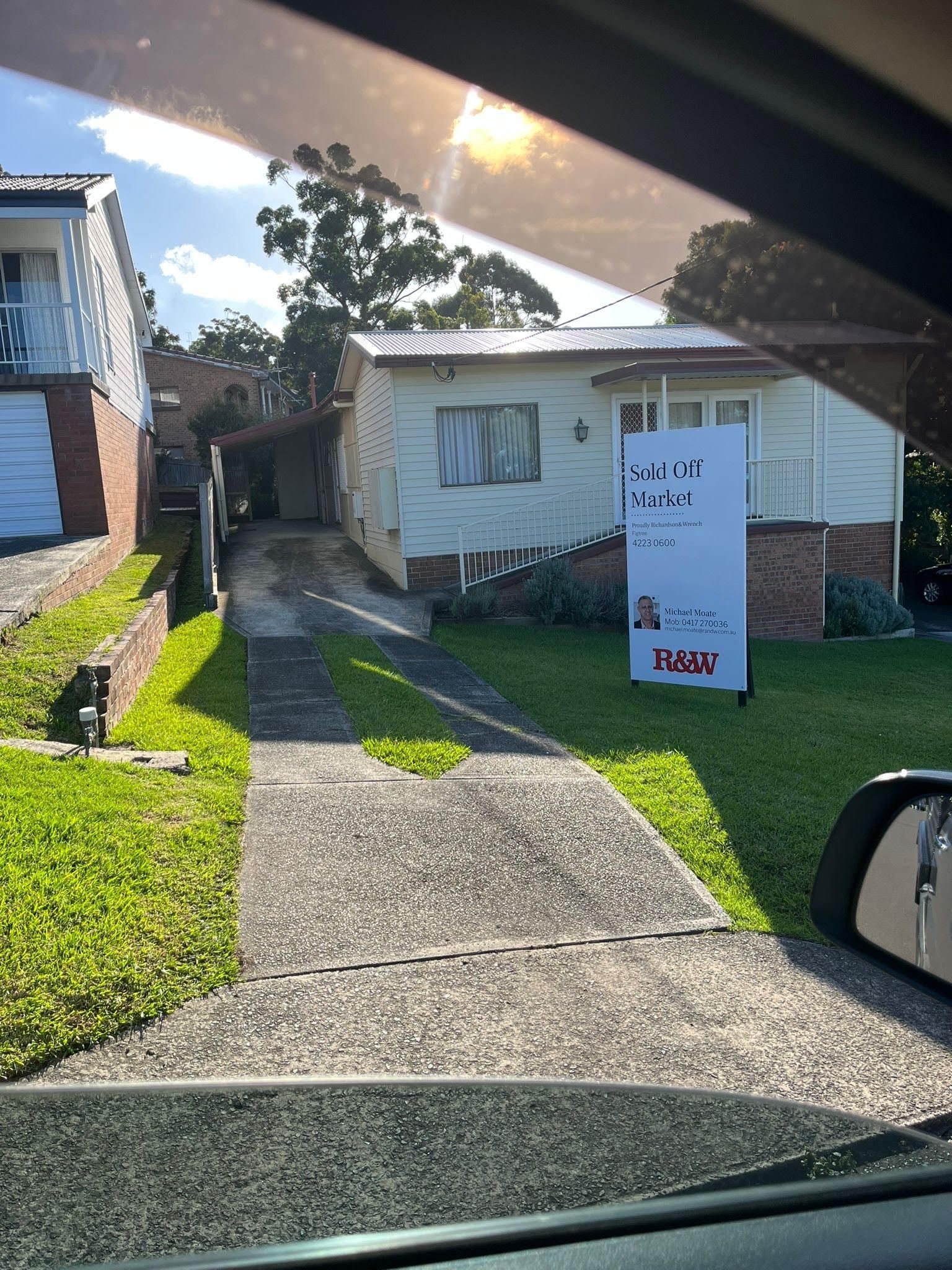 A house with peeling paint and a for-sale sign, viewed from a car window.