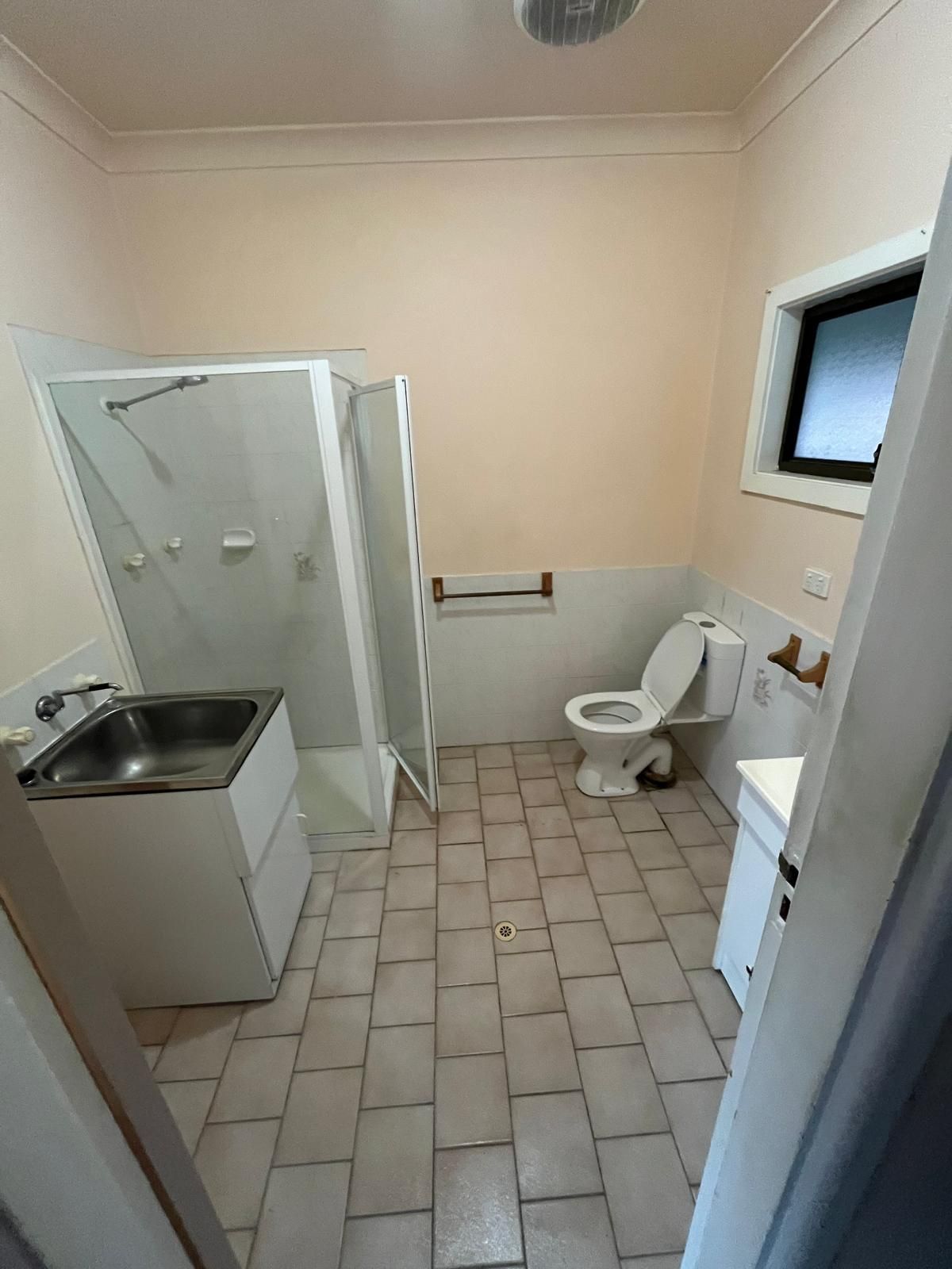 Bathroom with shower stall, sink, toilet, and window. Beige walls and tiled floor.