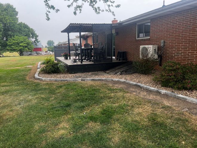 Brick house patio with black railing, stone border, and grassy yard on a cloudy day
