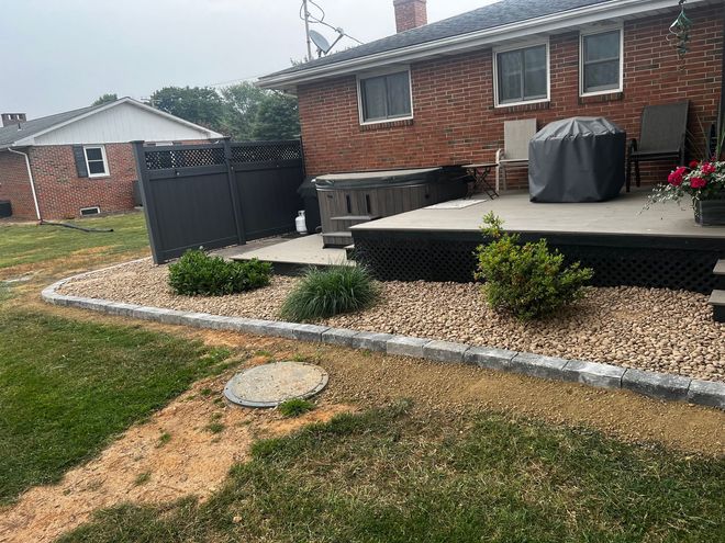 Backyard patio with brick house, black fence, grill, and landscaped gravel border.
