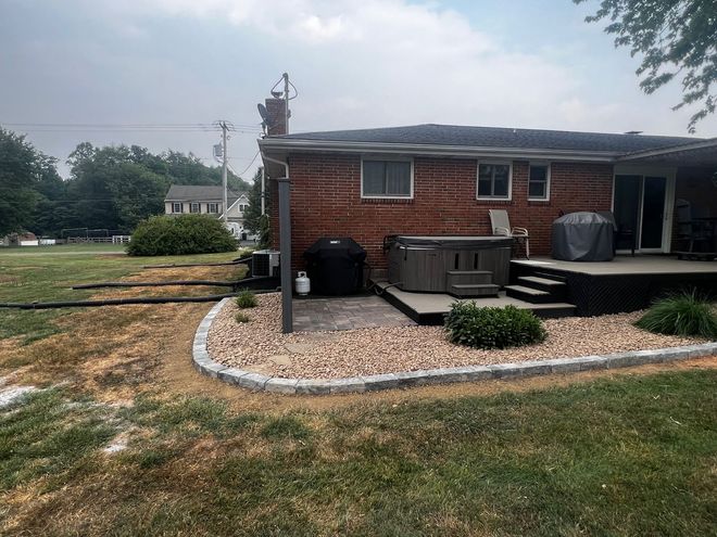 Brick house with small front deck, gravel border, and a black trash bin in a grassy yard