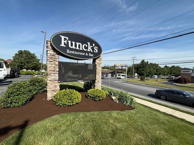 Funck’s Restaurant sign beside a roadside on a sunny day, with grass and landscaping.