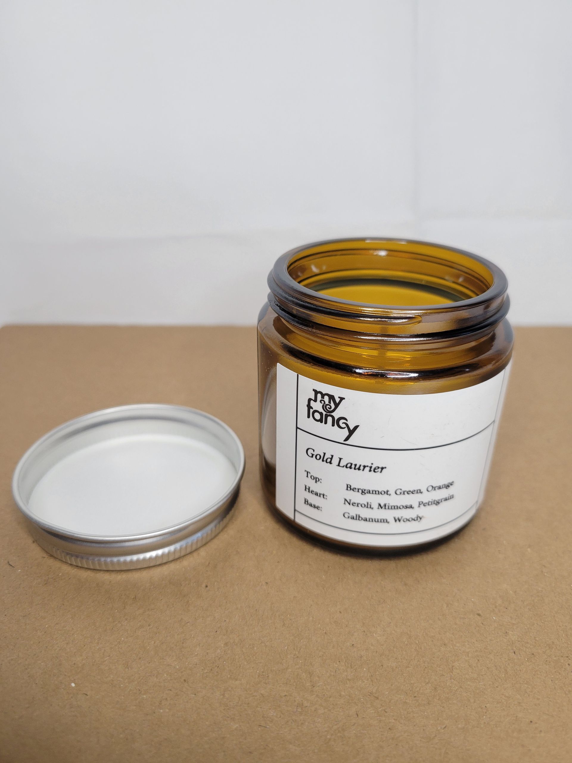 Open amber jar with white lid beside it on a cardboard surface, labeled container against a plain background