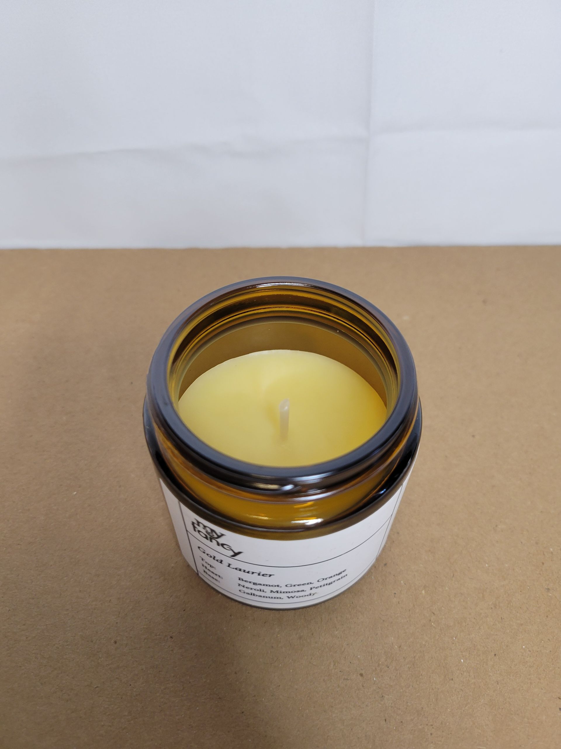 Open amber jar with white lid beside it on a cardboard surface, labeled container against a plain background