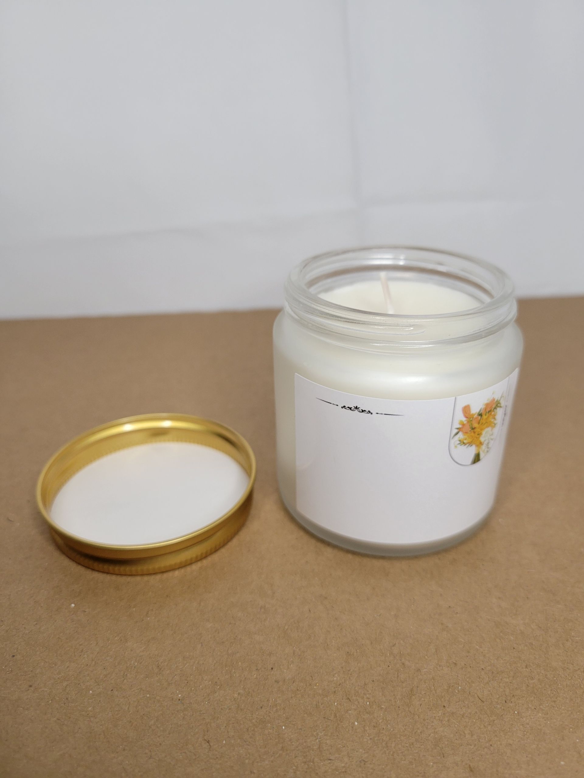 Open white candle jar with gold lid on a brown surface against a white background