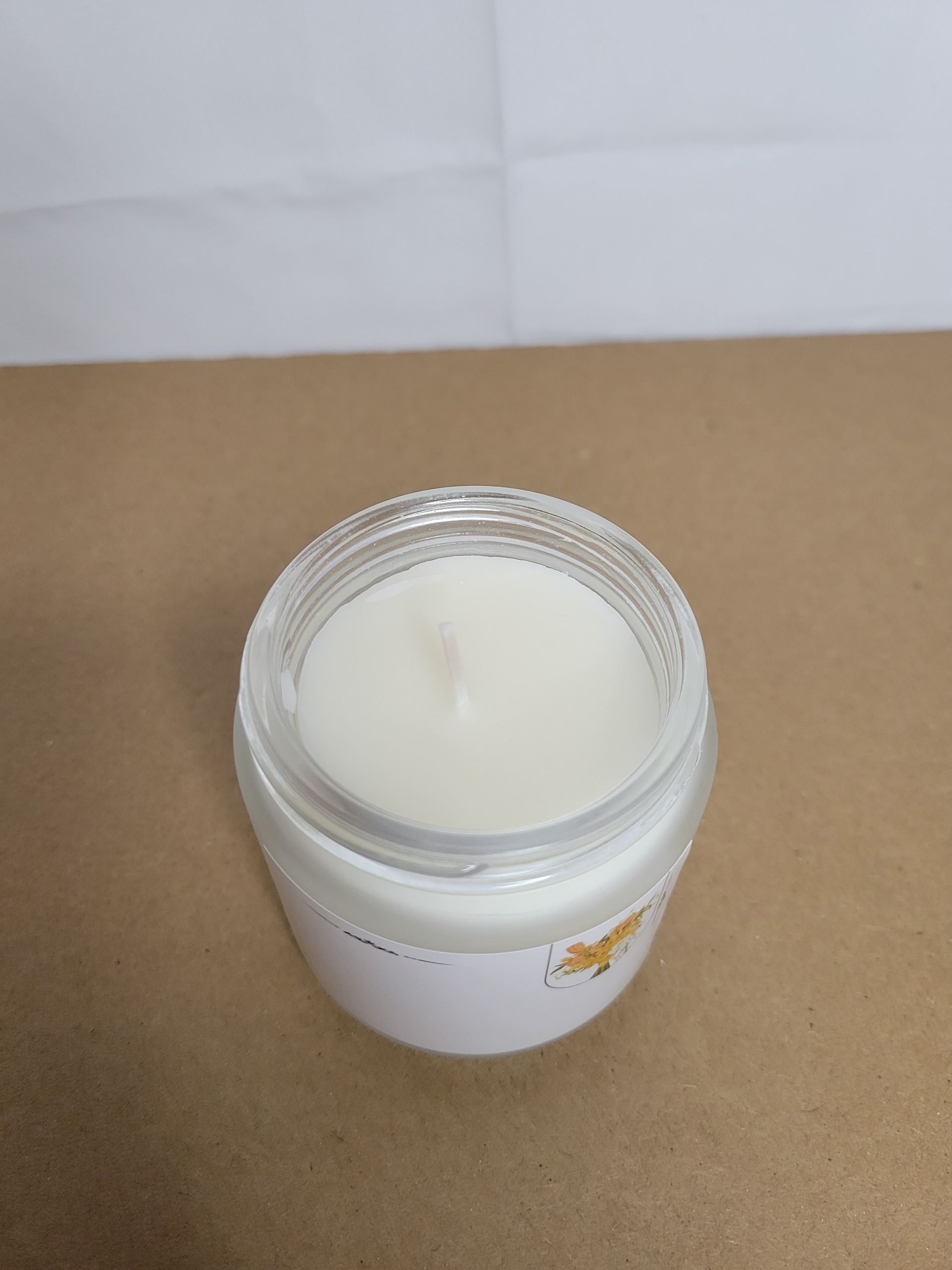 Open white candle jar with gold lid on a brown surface against a white background