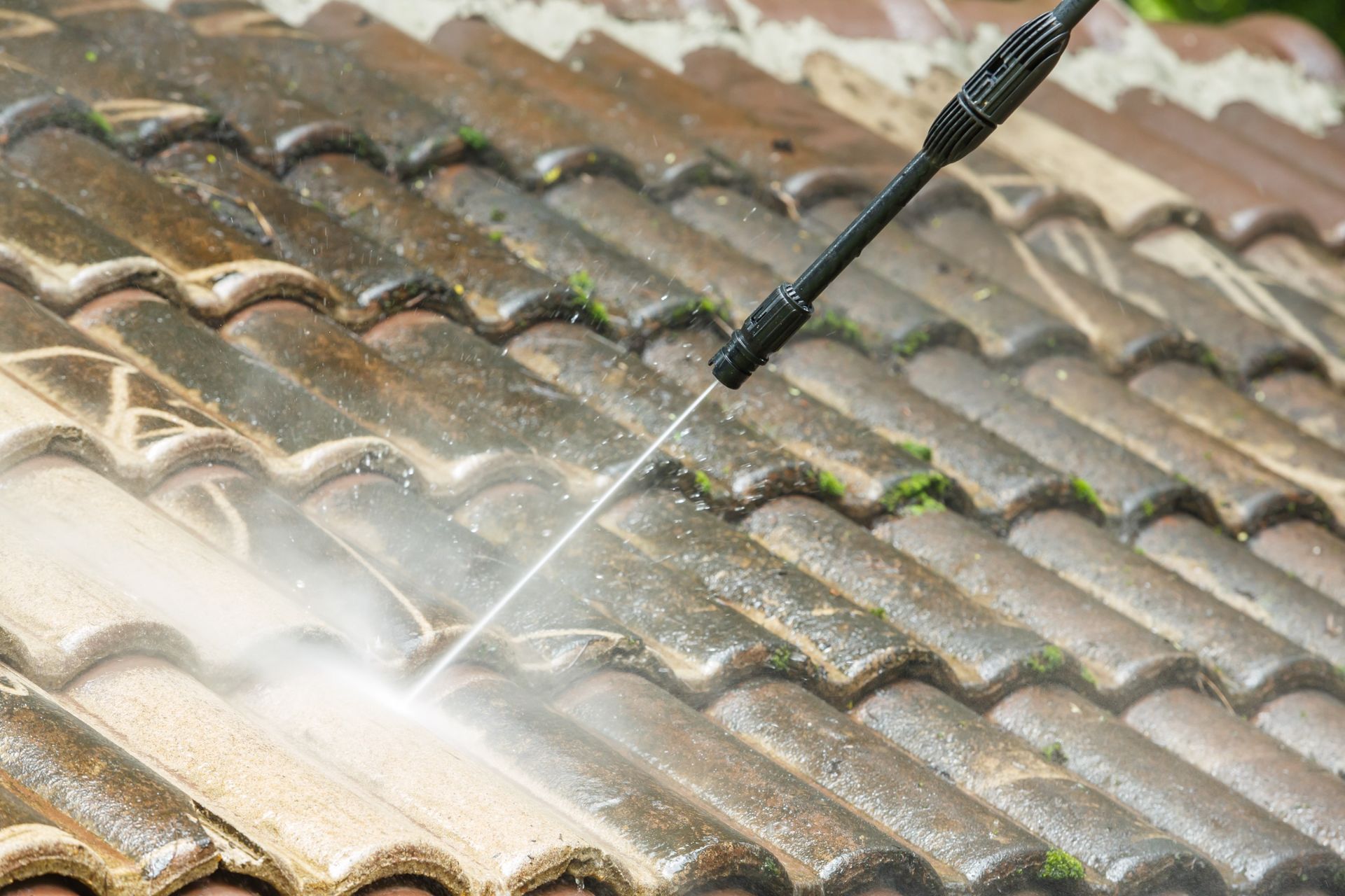 A person is cleaning a tiled roof with a high pressure washer.