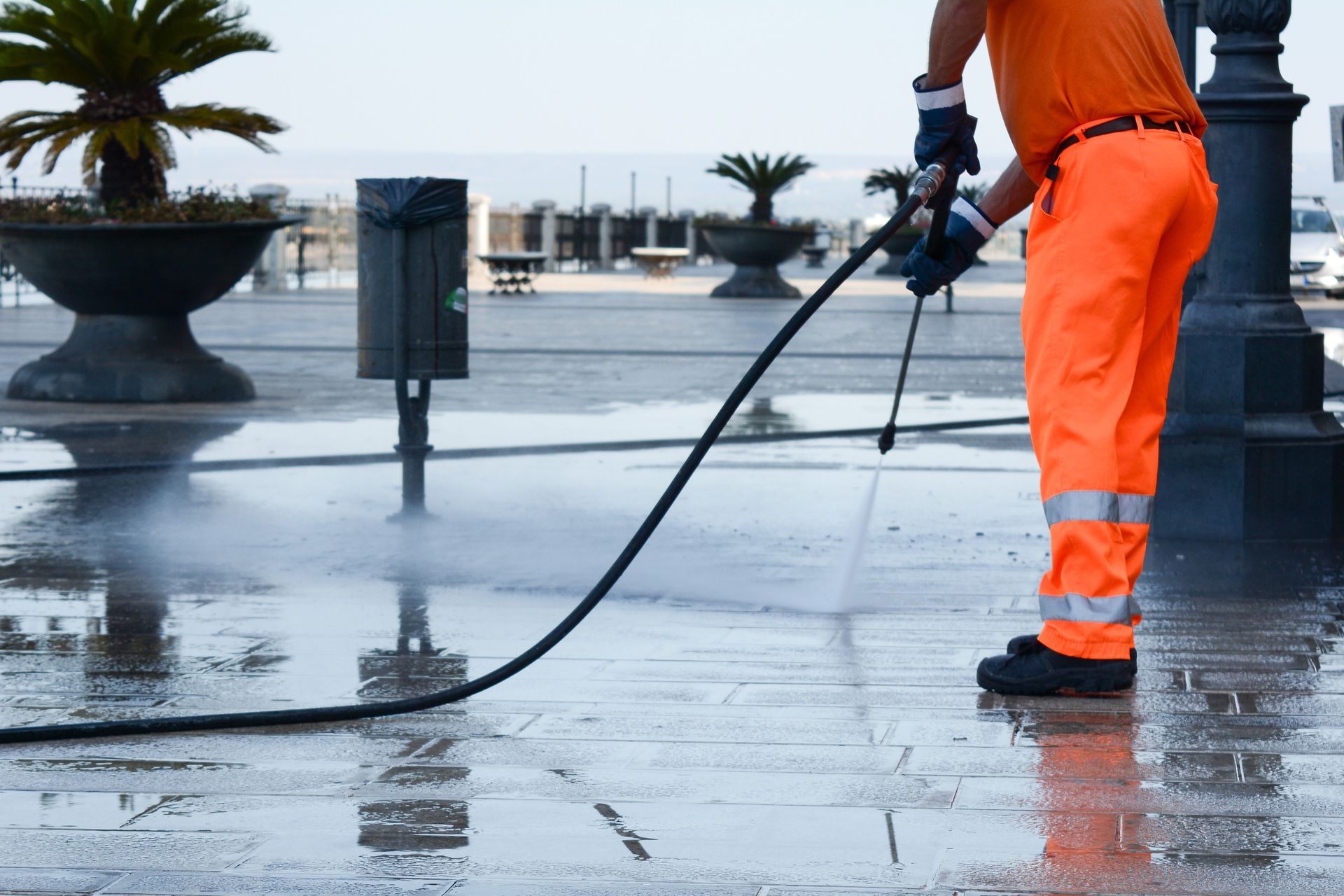 A man in orange pants is using a high pressure hose to clean a sidewalk
