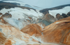 Colorful volcanic hills with white snow and pale blue ice under a cloudy sky
