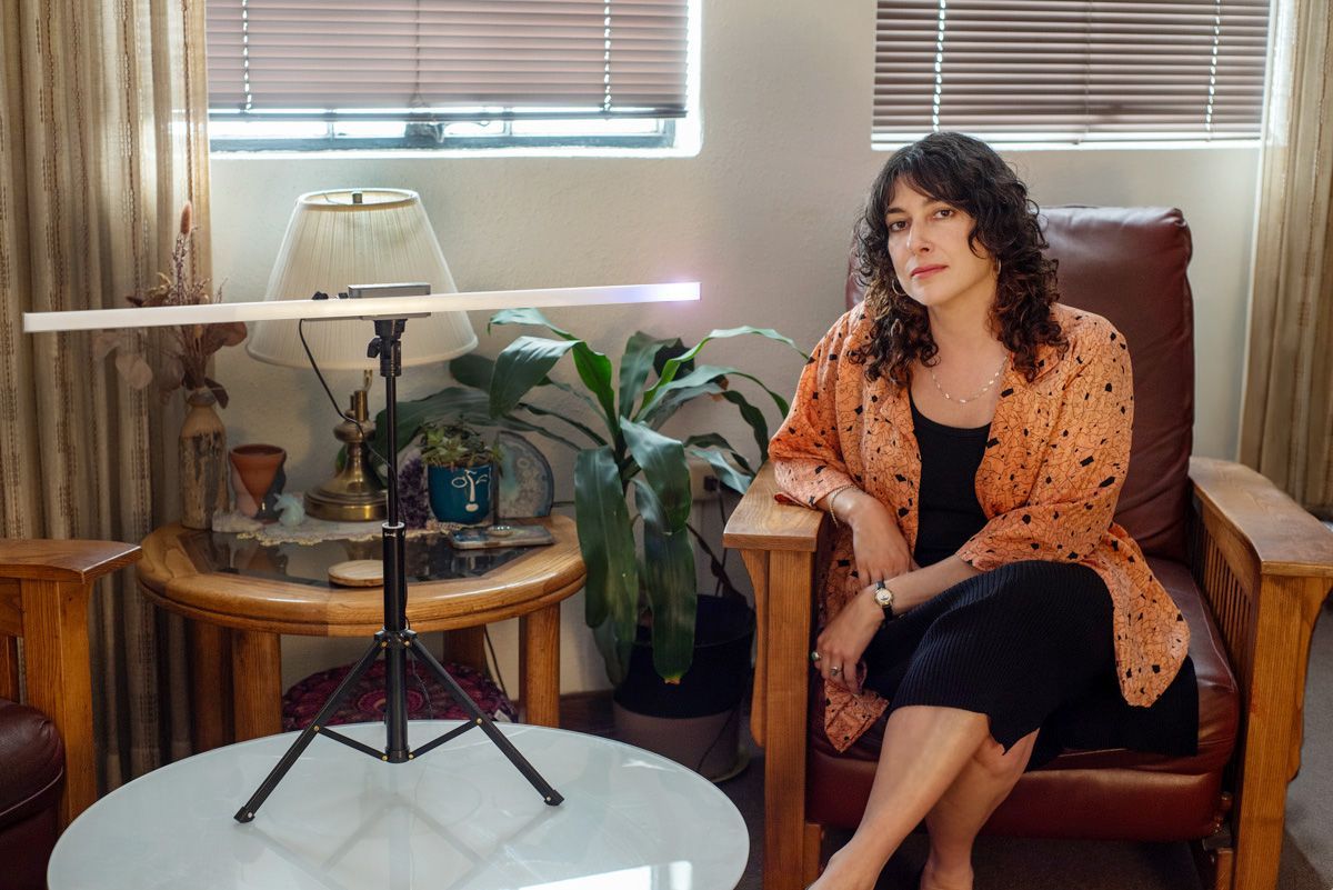 Woman seated in a leather armchair in a cozy living room beside a side table and plant.