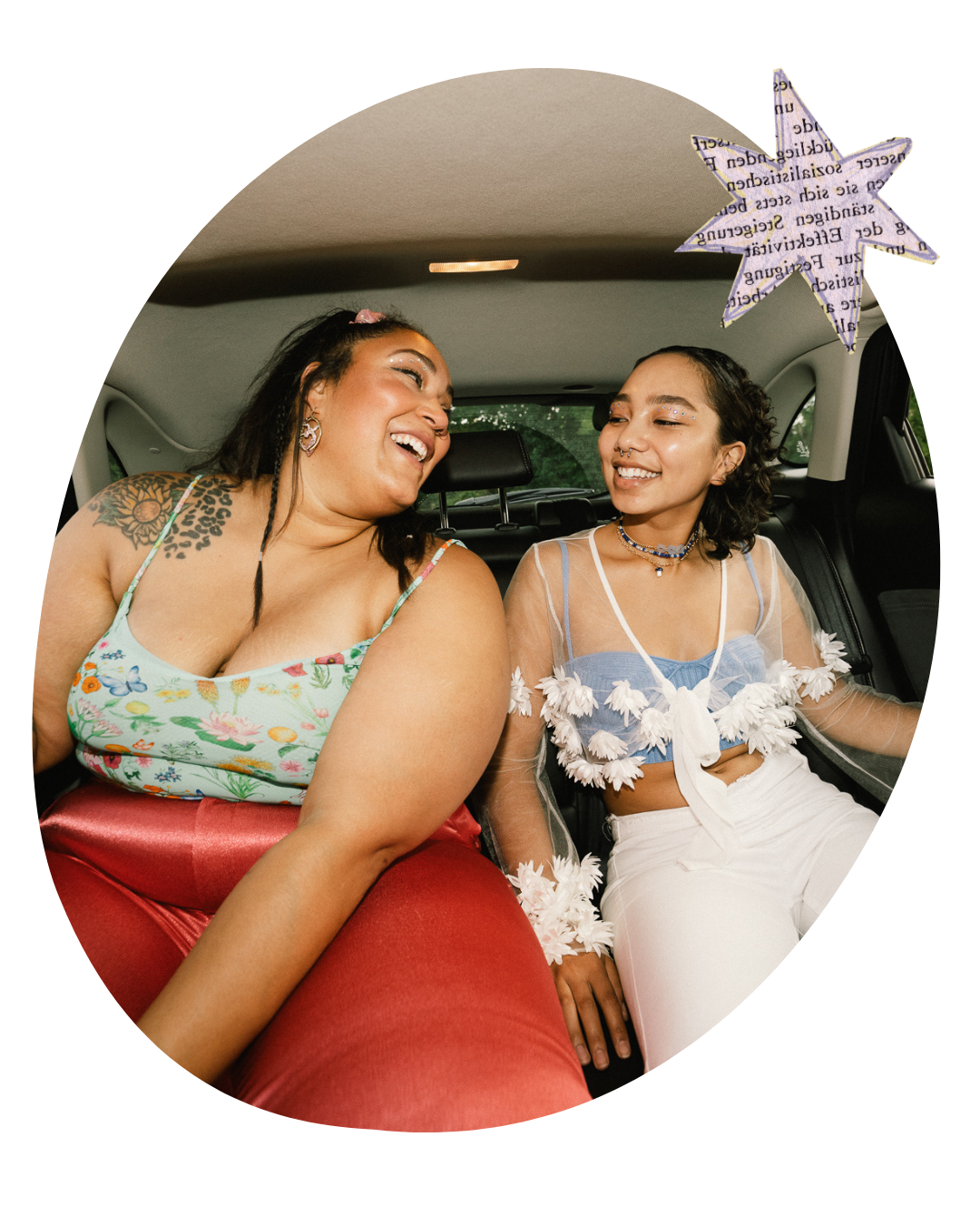 Two women smiling and laughing together in a car, one in a floral top and red skirt, one in white with a star decoration