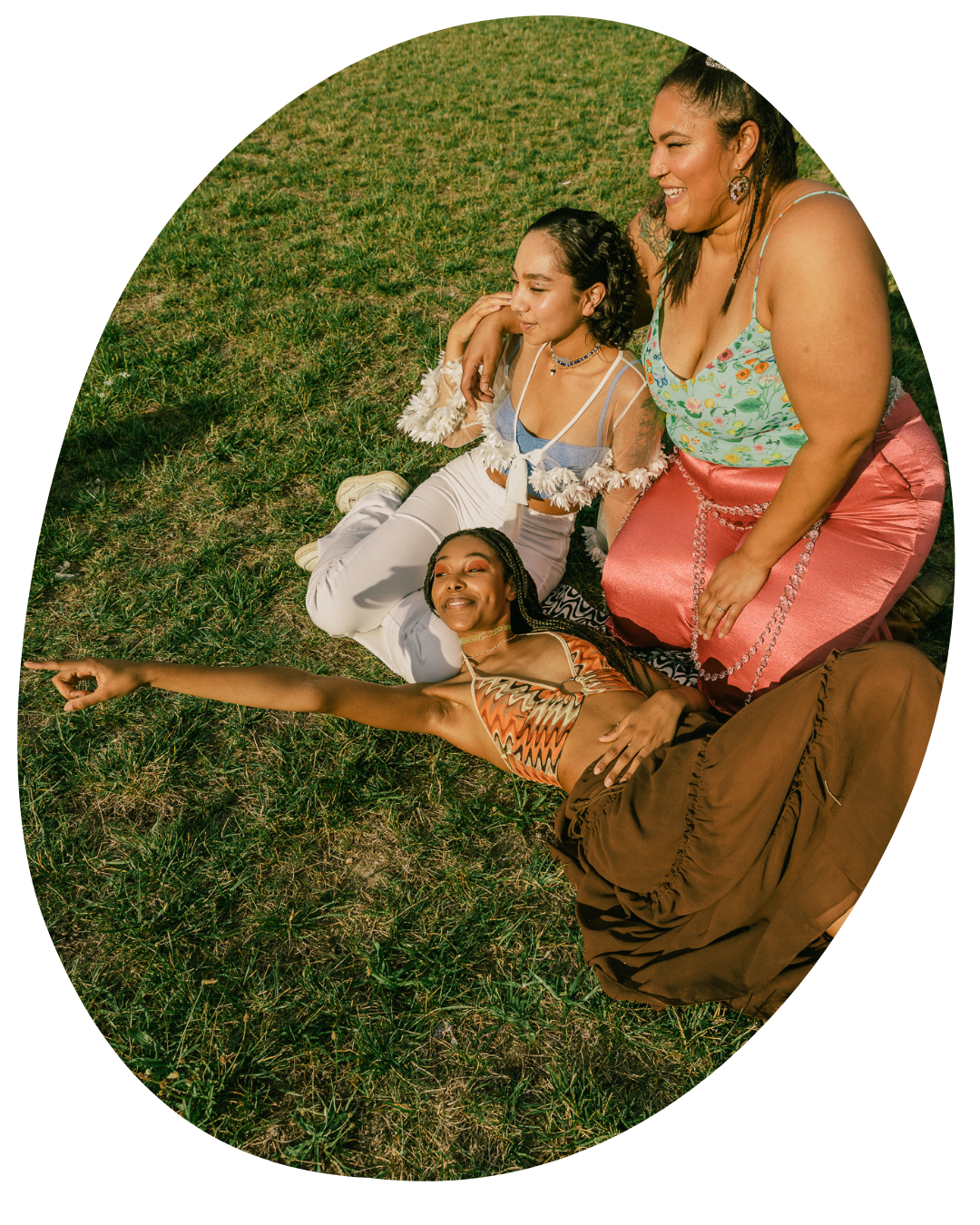 Three people lounging on grass, smiling and posing for a photo in warm sunlight.