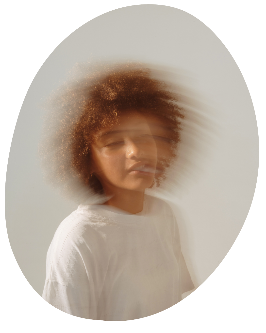 Soft-focus portrait of a person with curly hair in a white shirt against a light background