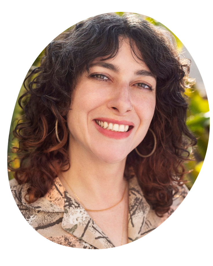 Smiling woman with curly dark hair in a light floral blouse, outdoors with greenery in the background
