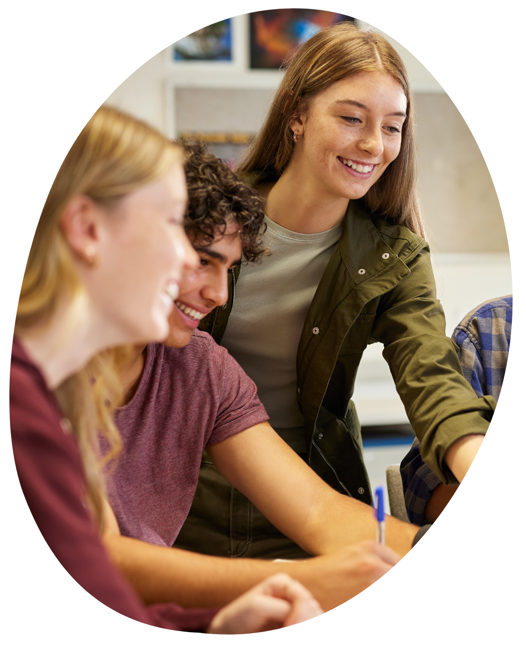 Students collaborating and smiling around a classroom table, with one writing in a notebook.