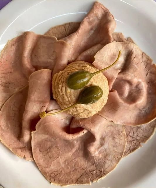 Roast beef tagliato a fettine sottili su un piatto bianco, guarnito con capperi e una fetta di limone