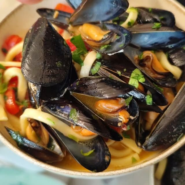 Ciotola di cozze al vapore con erbe aromatiche e verdure affettate in un brodo leggero