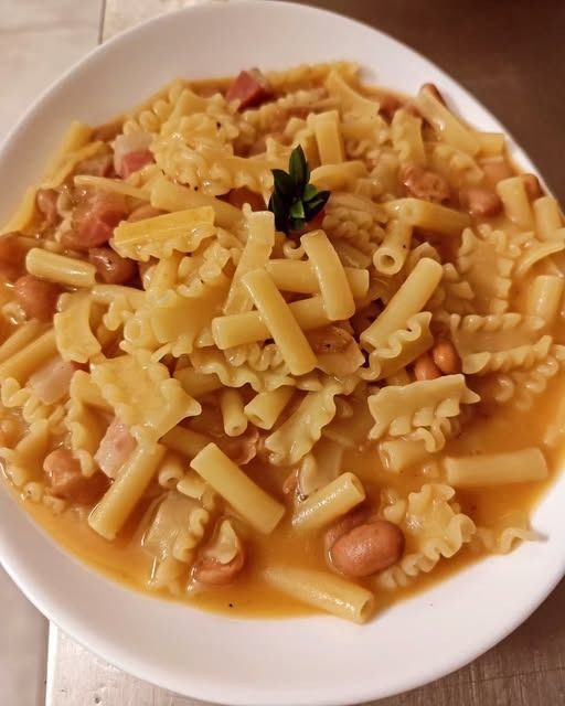 Pasta e fagioli in un brodo leggero all’arancia, servita su un piatto bianco e guarnita con una piccola quantità di erbe aromatiche