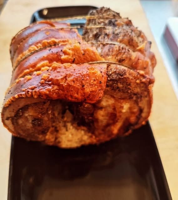 Pancetta di maiale arrosto con cotenna croccante e dorata su un vassoio nero