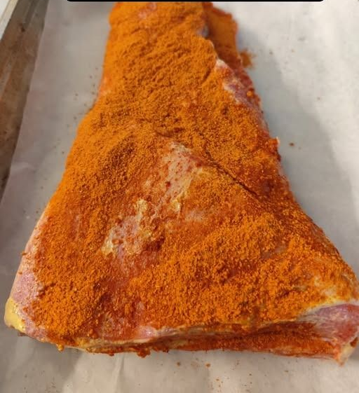 Punta di petto triangolare ricoperta di condimento rosso-arancio su un vassoio, con l’etichetta «Preparazione brisket»