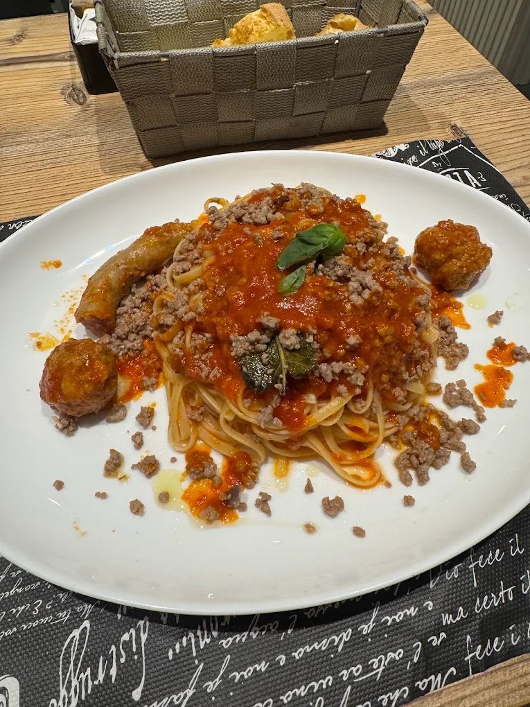 Pasta condita con un ricco ragù di carne su un piatto bianco, con un cestino di pane sullo sfondo.