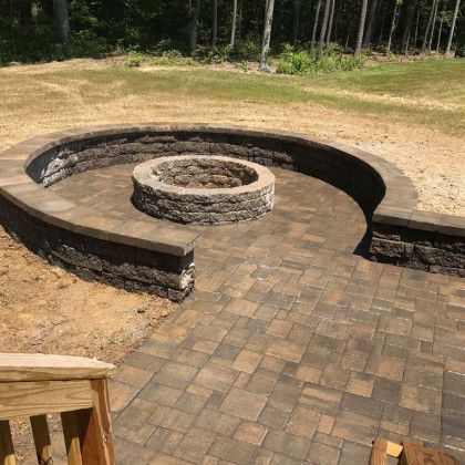 Stone fire pit and curved wall on a brick patio in a grassy outdoor setting.