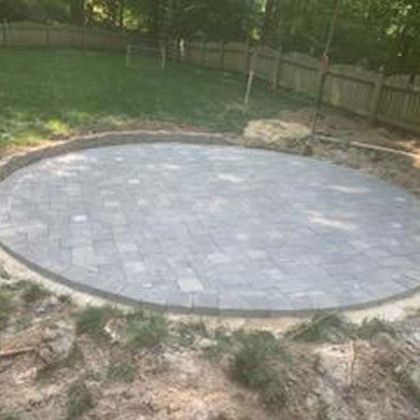 Circular paved patio under construction in a grassy yard. Gray pavers and border.
