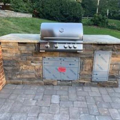 Outdoor kitchen with a stainless steel grill built into a stone structure.