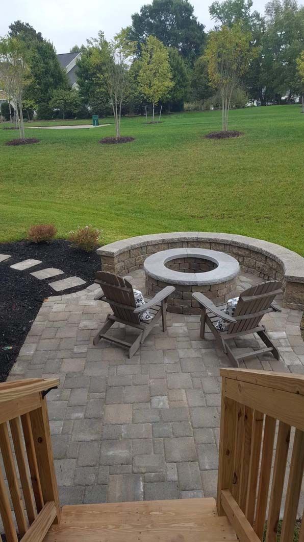 Patio with fire pit, two chairs, and a grassy backyard. Wooden stairs lead down.