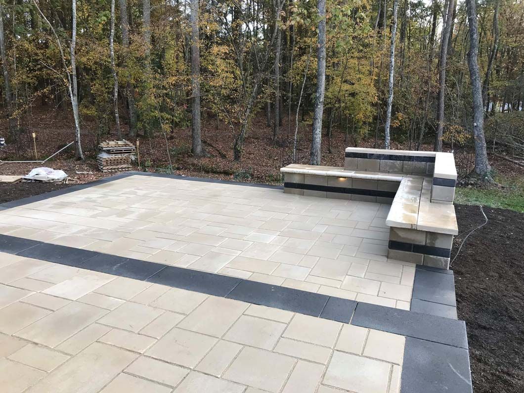 Outdoor patio with stone pavers, built-in benches, and dark border. Forest background.