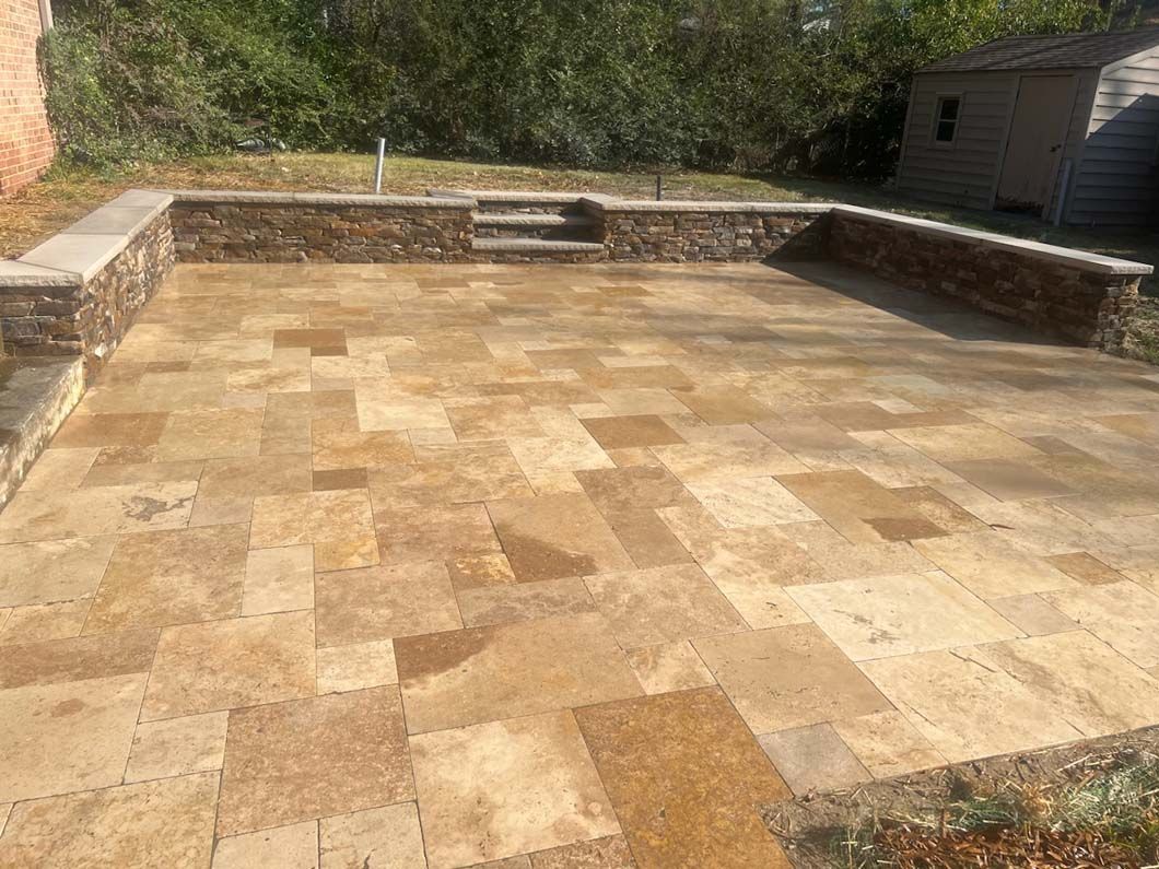 A stone patio with a low stone wall in a backyard setting.