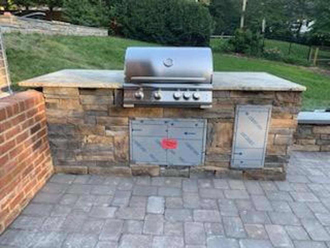 Outdoor stone grill with stainless steel grill and cabinet doors, built on a brick patio.