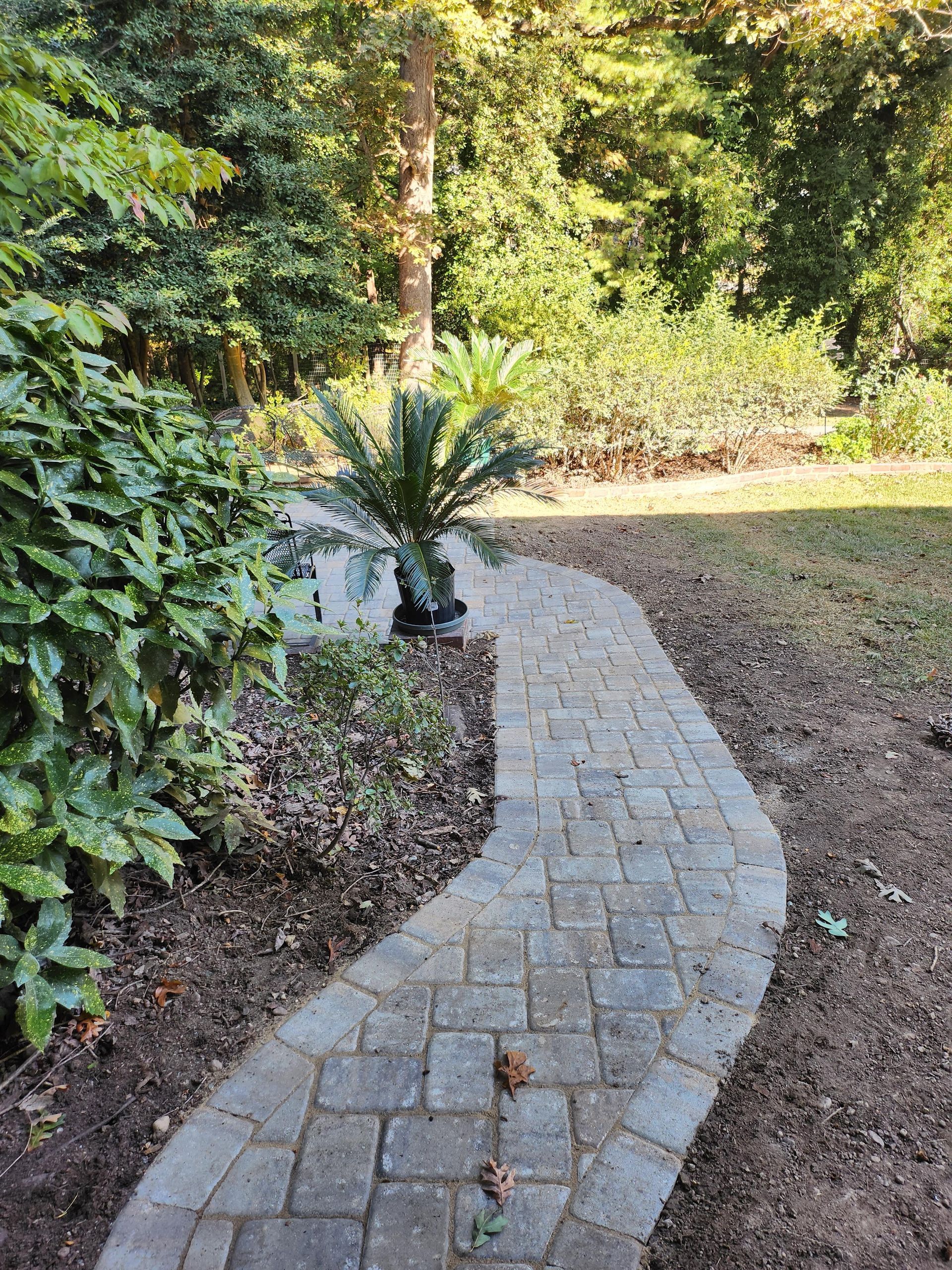Brick path winds through a garden, with greenery on either side.