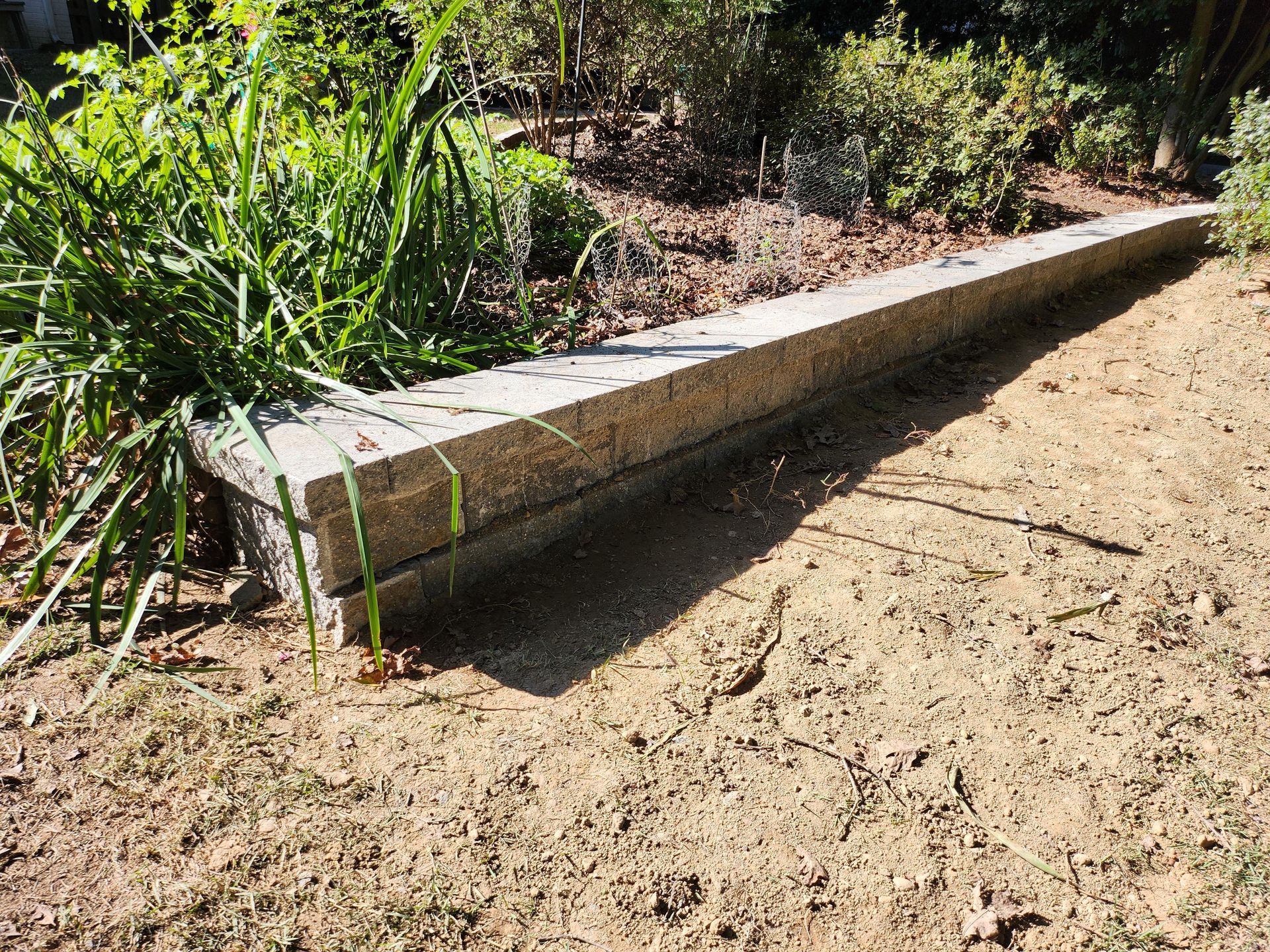 A long, gray stone planter box with overgrown greenery in a garden setting.