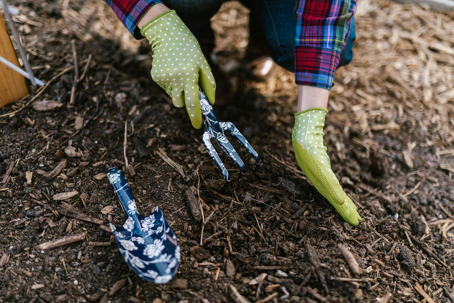 Person wearing green gloves using a hand fork in a garden bed.