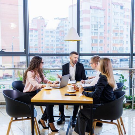 Three people meeting at a round table in a bright café with large windows and city views