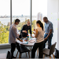 Team collaborating around a table in a bright office with a city and water view.